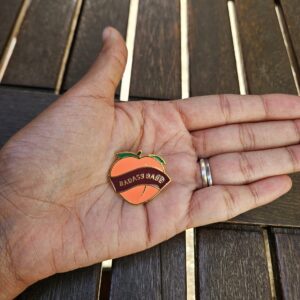 Pin's pêche "Badass Babe" dans la paume d'une main pour visualiser les proportions