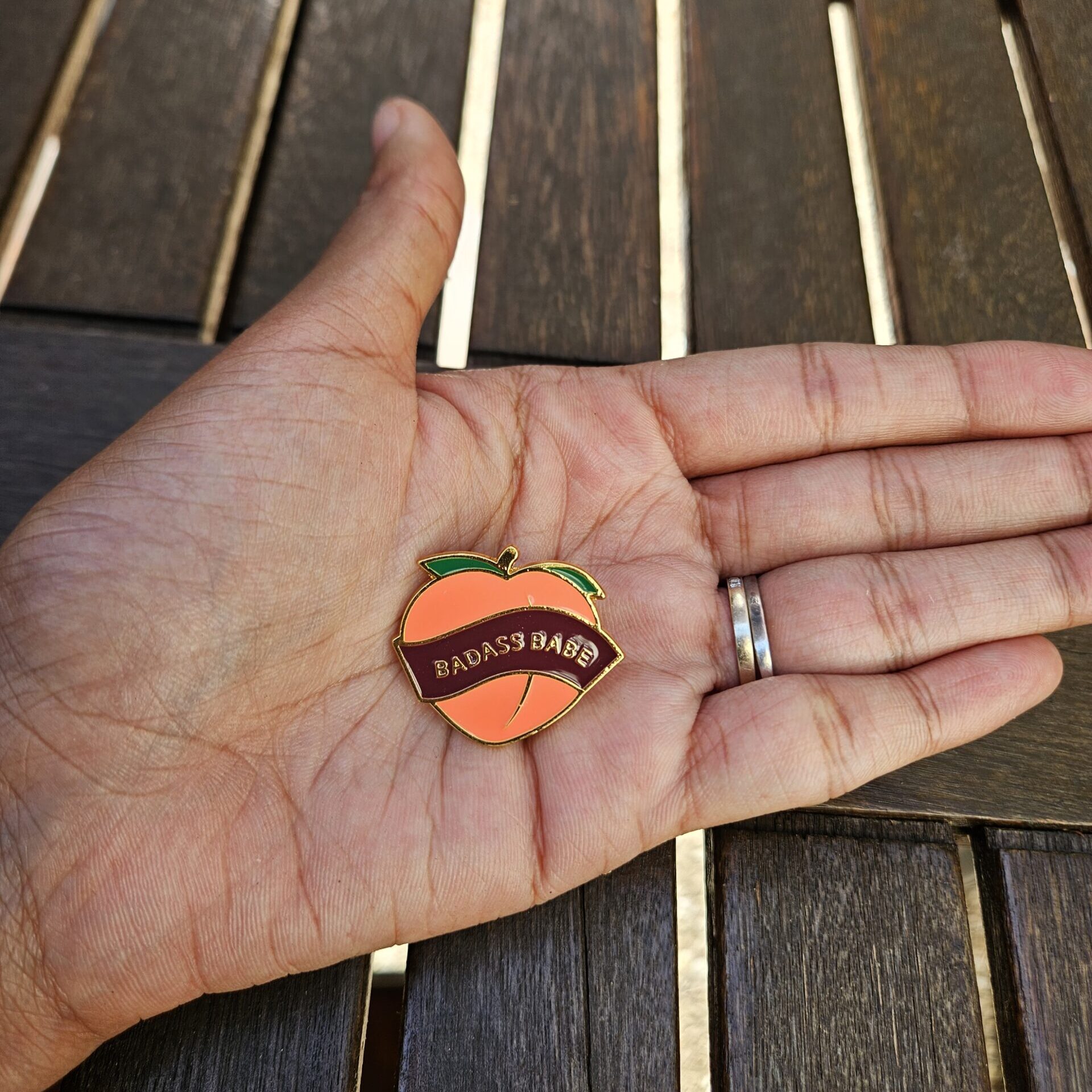 Pin's pêche "Badass Babe" dans la paume d'une main pour visualiser les proportions