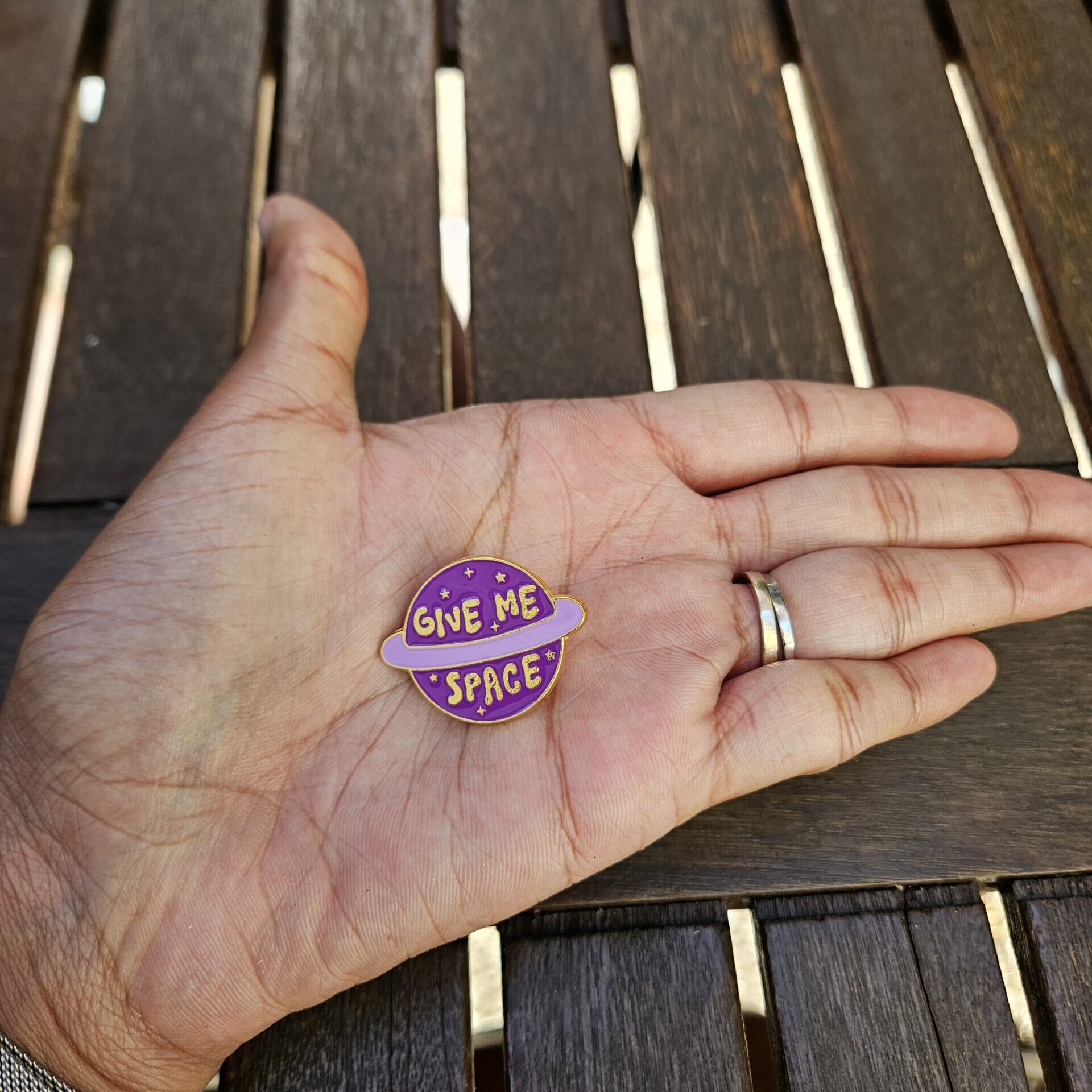 Pin's planète violète "Give me space" tenu dans la paume d'une main afin de visualiser les proportions