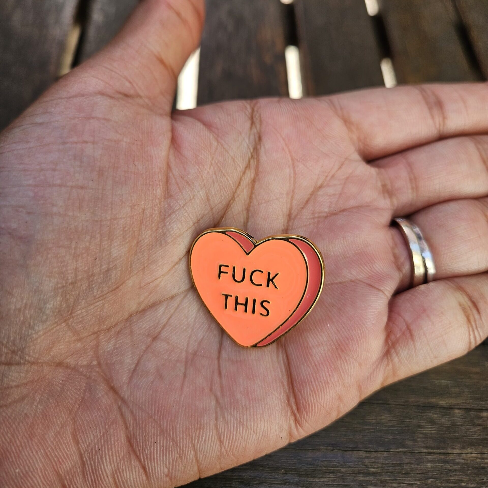 Pin's coeur orange "Fuck this" dans la paume d'une main pour visualiser les proportions